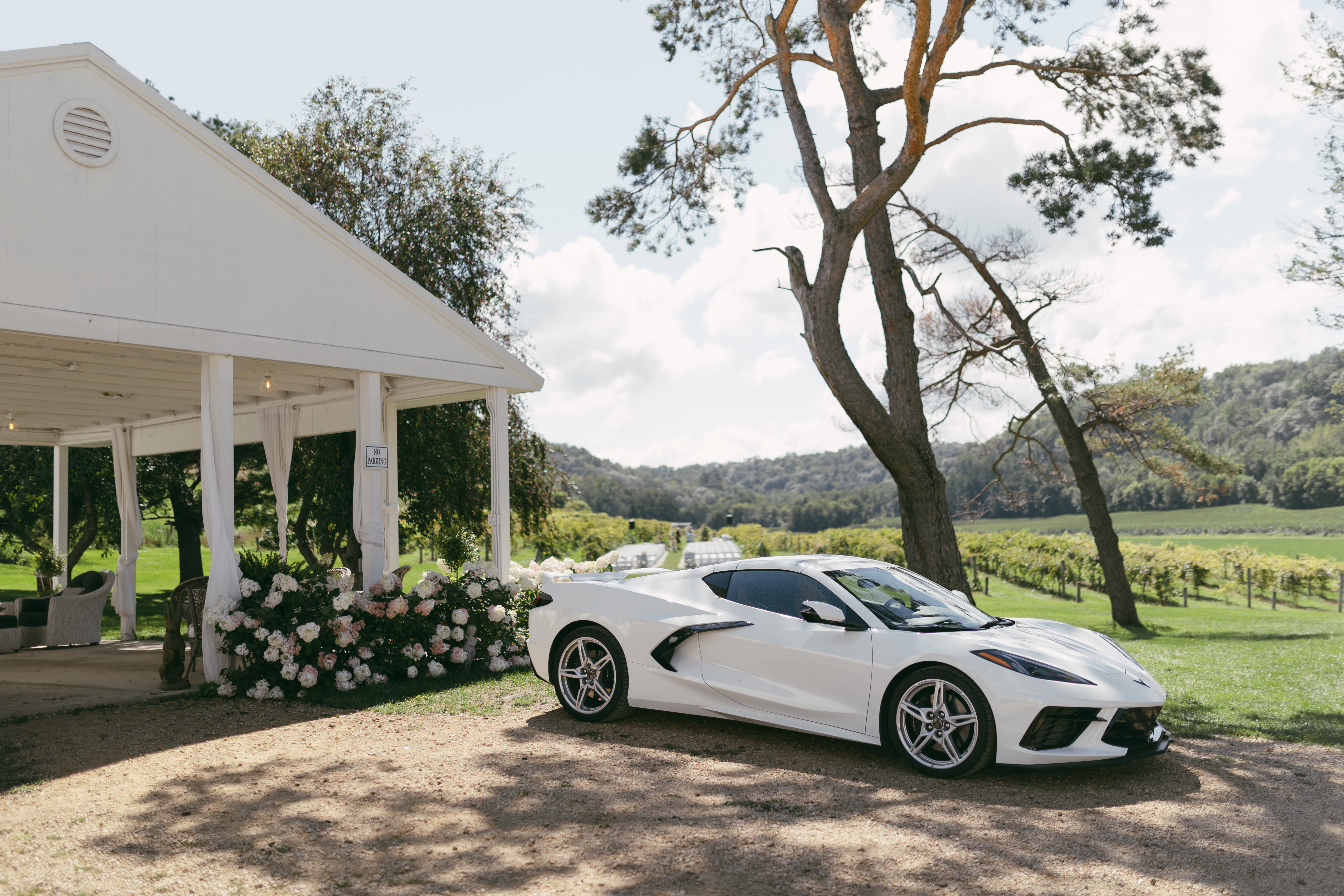 A white 2023 Chevrolet Camaro convertible parked in front of a venue awning, serving as the couple's wedding exit car. The classic sports car is positioned and ready for the newlyweds' departure from their wedding celebration.